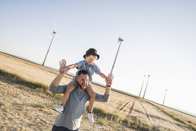 Father carrying son on shoulders in front of wind turbines