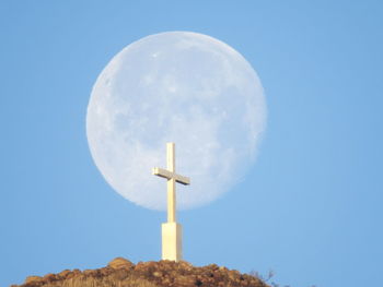 Low angle view of cross against blue sky with setting moon. 