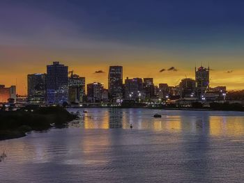 Illuminated city at waterfront during sunset