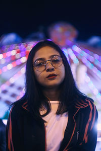 Portrait of young woman standing against illuminated ride