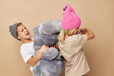 Sibling playing with stuffed toy against beige background