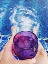 Low section of woman holding drink in swimming pool