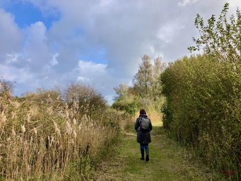 Rear view of woman walking on field against sky