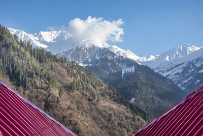 Snow mountain with nice sun rays, clouds and red roof of house.