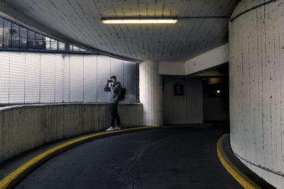 Side view of young man with backpack photographing while standing by window