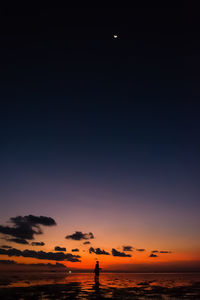 Silhouette woman standing in sea against sky during sunset