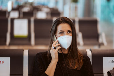 Woman wearing mask talking on phone while sitting at airport