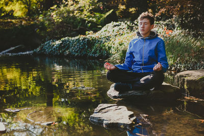 Teenage boy meditating and relaxing in a city park japanese garden. outdoor meditation