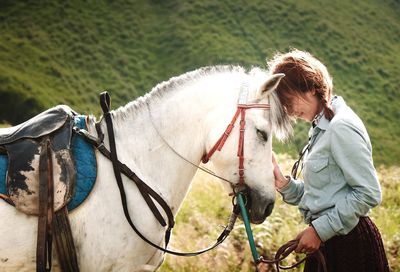 Side view of woman standing face to face with horse on field