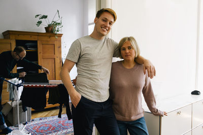 Portrait of smiling son with arm around parent standing at home