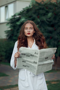 A lady with red lips and a chic hairstyle is holding a newspaper in the street. white housecoat