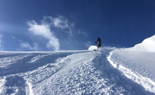 Man skiing on snow covered landscape against blue sky