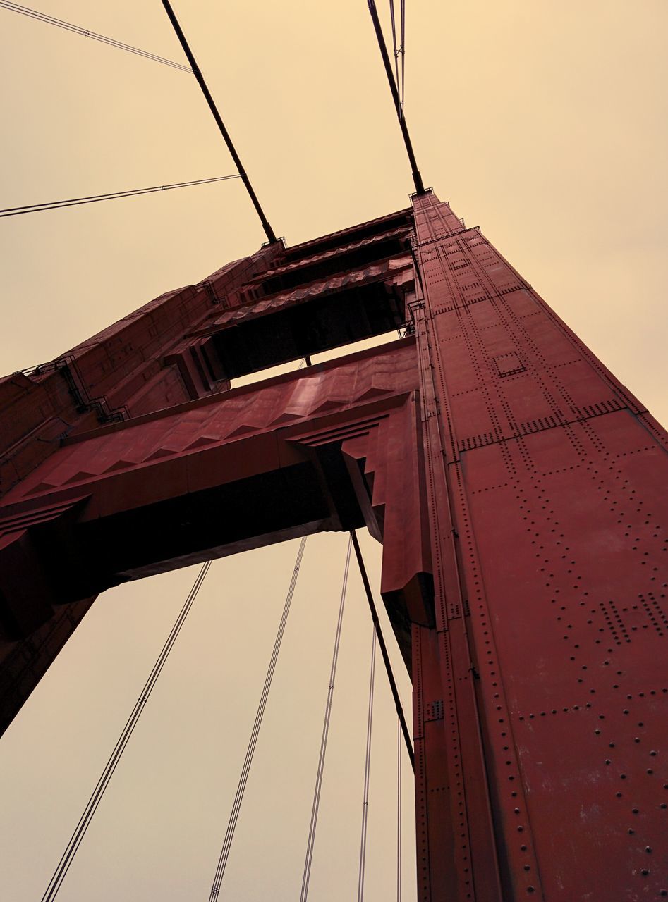 low angle view, architecture, built structure, clear sky, connection, building exterior, sky, cable, power line, outdoors, tall - high, bridge - man made structure, no people, day, engineering, silhouette, city, tower, development, high section