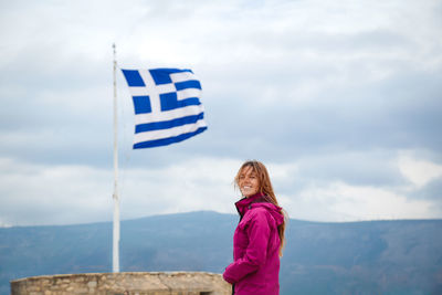 Smiling woman standing by flag against sky