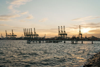 Oil platforms at pier against sky during sunset