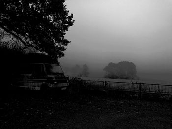 Silhouette trees by calm sea against sky during foggy weather