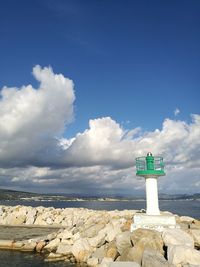 Lighthouse amidst rocks and buildings against sky