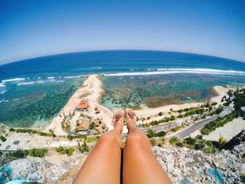 Low section of sensuous woman on rock formation by sea against clear sky