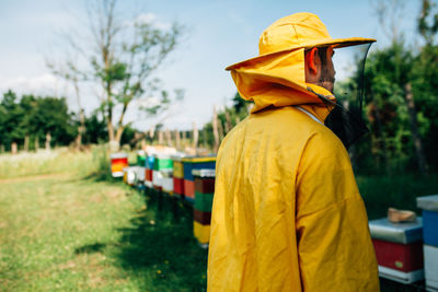 Side view of beekeeper standing by beehives on land