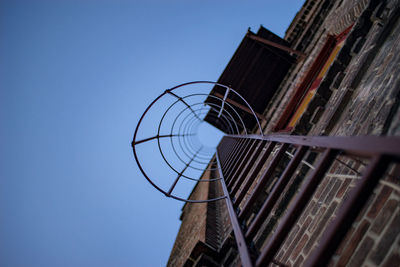 Low angle view of ladder amidst building against clear sky