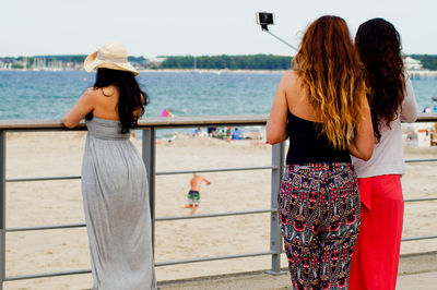 Rear view of female friends taking selfie by woman at beach against sky