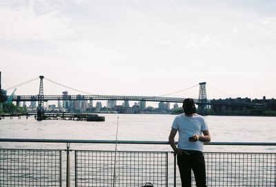 Man standing on bridge over river against sky