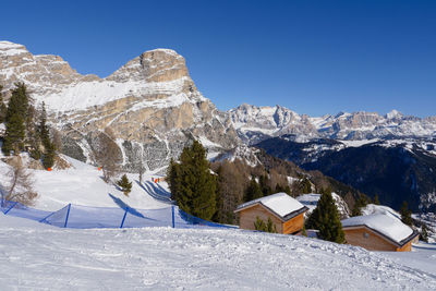 Mountain houses with snow on their roofs and fir trees full of snow, italian alps in the background.