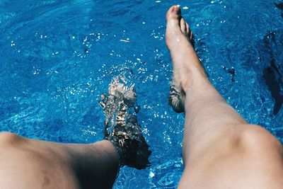 Low section of woman dangling legs in swimming pool