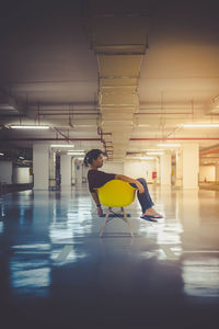 Full length side view of woman sitting on yellow chair in parking garage