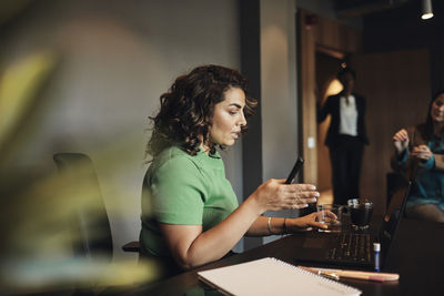 Side view of businesswoman gesturing while discussing with colleagues in office