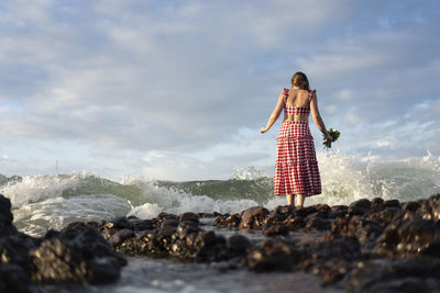 Woman standing on rock by sea against sky