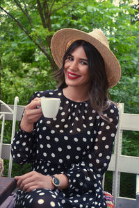 Portrait of smiling young woman drinking coffee while sitting at porch 