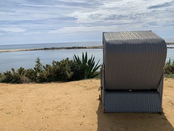 Hooded beach chair by sea against sky