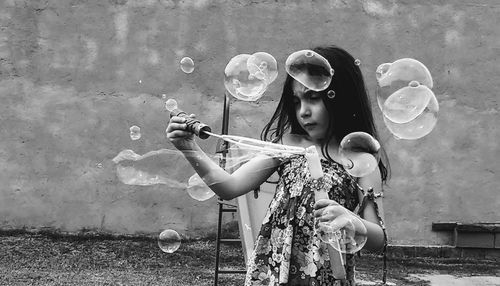 Low angle view of girl playing with bubbles against wall