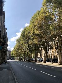 Road by trees in city against sky