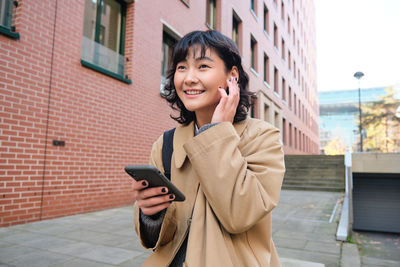 Portrait of young woman standing against building