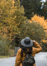 Rear view of woman with backpack, walking on road through autumn woods