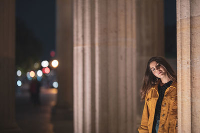 Portrait of woman standing against pillar at night