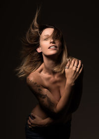 Shirtless woman with tousled hair against black background