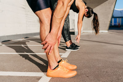 Side view of fitness couple in sportswear doing forward bends during training in city on summer day