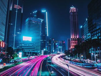 Light trails on road amidst illuminated buildings in city at night