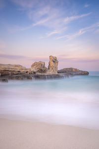 Rock formations on beach against sky during sunrise