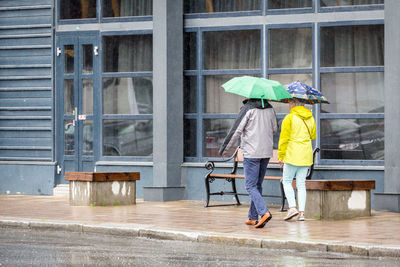 Rear view of friends with umbrellas walking on sidewalk in rain