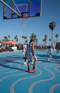 People playing basketball by swimming pool against sky