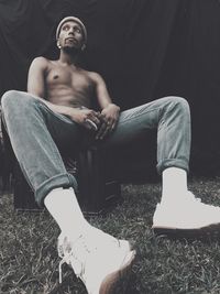 Full length of thoughtful shirtless man sitting on crate outdoors