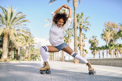 Portrait of mid adult woman with arms raised roller skating against blue sky