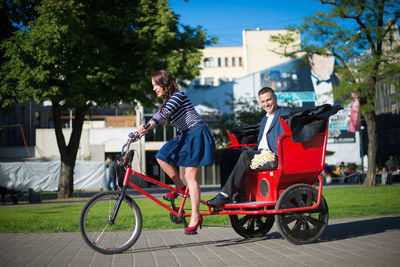 Man and woman traveling in pedicab on street during sunny day