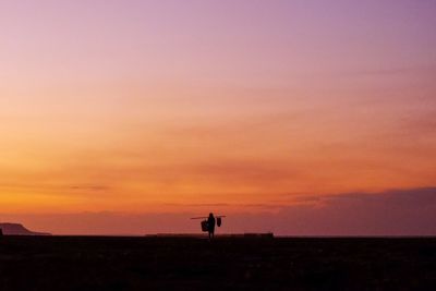 Silhouette people standing on field against sky during sunset