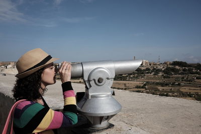 Woman looking through coin-operated binoculars against sky