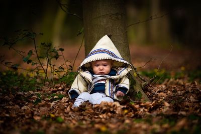 Cute newborn boy relaxing against tree on leaves covered field during autumn